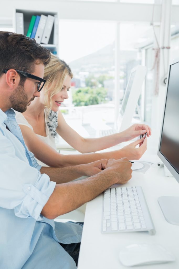 Side view of smiling casual young couple working on computer in a bright office